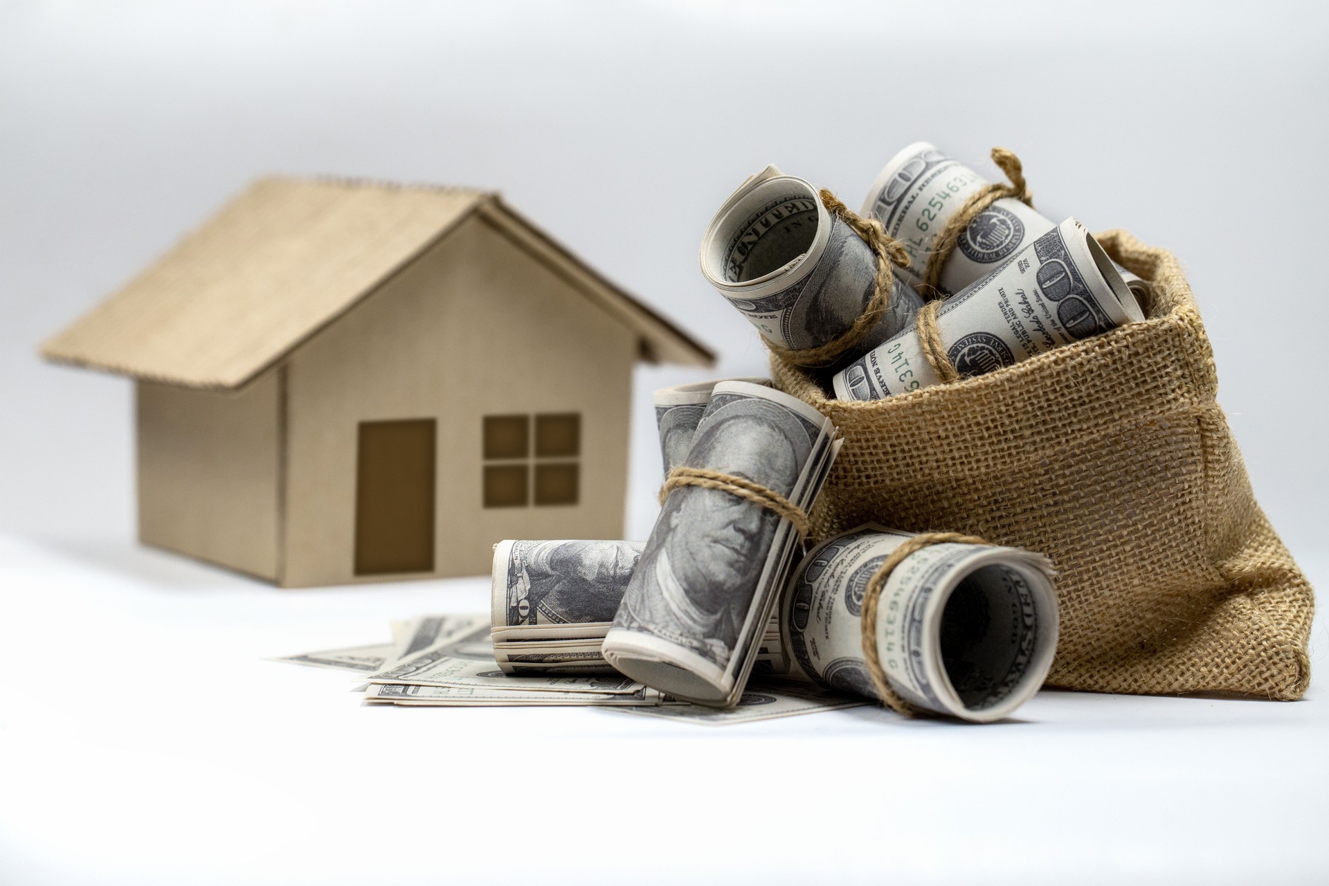 Roll of 100 US dollar bills Overflowing hemp sack and a house model on background.
